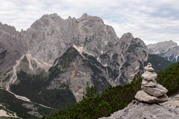 Cairns of stones trail marker indicates hiking trail to mountain peak Spik surrounded by rugged ridges of Julian Alps seen from Krnica valley, Vrsic, Slovenia. Wanderlust in wilderness, Slovenian Alps