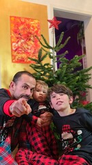 Family of man and 2 kids at home in front of the Christmas tree
