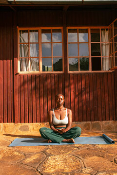 A young African woman practicing yoga stretching and meditation at home outdoors on a sunny day