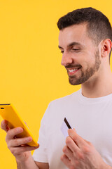 Man holding a smartphone and credit card against a bright yellow background.