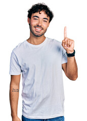 Naklejka premium Hispanic young man with beard wearing casual white t shirt pointing finger up with successful idea. exited and happy. number one.