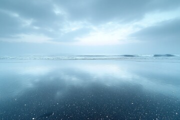 Obraz premium Serene beach seascape at dawn, with calm waves mirroring the cloudy sky on wet sand.
