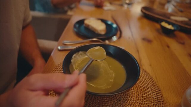 Close up of man slurping butternut squash soup at dinner table, eating appetizer with cozy restaurant ambiance