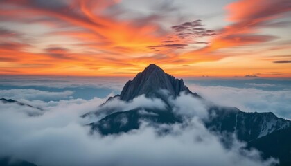 Majestic mountain peak surrounded by clouds at sunset, showcasing vibrant colors in the sky.