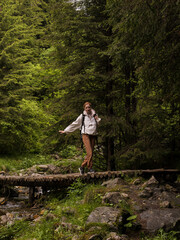 Fototapeta premium Woman crossing bridge over the river in thick woods. Females adventure in the forest finding a river with a wooden bridge. Holidays activity inspiration.