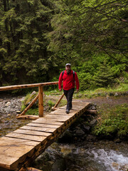 Fototapeta premium Man sitting on a bridge and admiring nature, river and dense forest. Man ventures into the forest finding a river with a wooden bridge. Inspirational holiday activity.