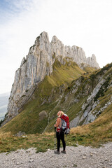 Fototapeta premium Young woman with backpack hiking in Appenzell Innerrhoden canton of Swiss Alps, Switzerland. Rocky mountain peaks on the background