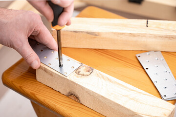 Carpenter using a screwdriver to attach a metal bracket to wooden planks, demonstrating woodworking...