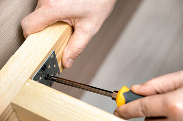 Close-up of a carpenter's hands tightening a screw into a wooden frame with a screwdriver and metal...