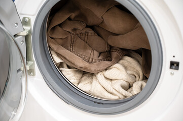 Clothes inside a washing machine drum with beige pants and cream-colored sweater ready for laundry
