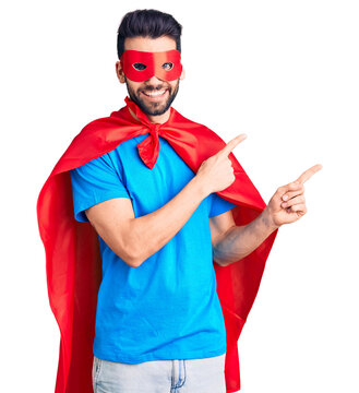 Young handsome man with beard wearing super hero costume smiling and looking at the camera pointing with two hands and fingers to the side.