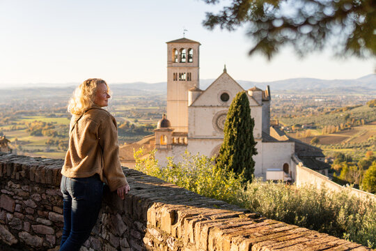 Young woman enjoying the view of Basilica of St. Francis in Assisi hilltop town of Umbria, Italy.