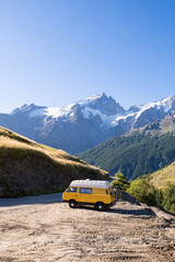 Yellow retro camper van exploring the Alps with high mountains in the background, Ecrins national park, France