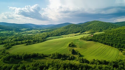 Obraz premium Lush Agricultural Fields Nestled Amongst Rolling Green Mountains Under a Dramatic Sky