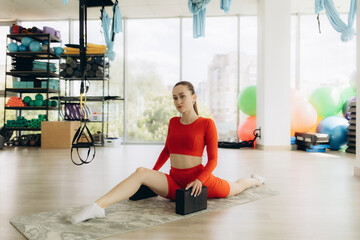 A young woman is depicted sitting on a yoga mat in a well-lit studio. She is dressed in black...