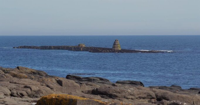 Extra Wide shot of little carr rock with rocks in foreground at Craster