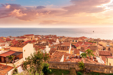 wonderful landscape of beautiful mediterranean sunset town in Italy with orange old tile roofs, nice sea gulf coast, calm evening water and awesome yellow cloudy sky on background