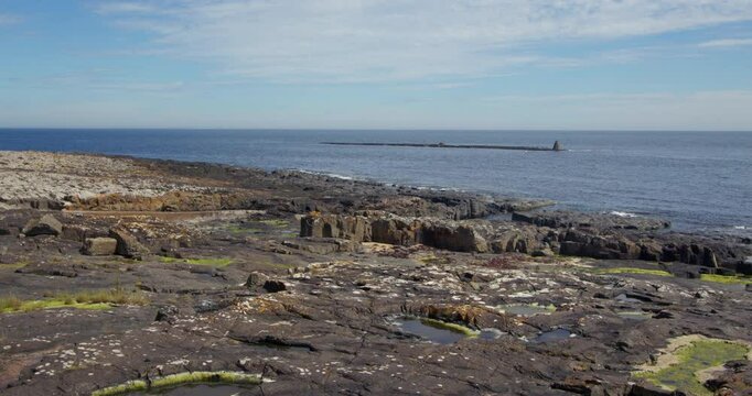 extra wide shot of the exposed rocks at Craster harbour at with little carr in background