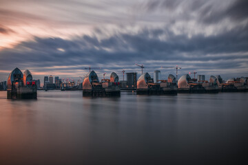 The London Thames Barrier under a dramatic sunset sky, with city in the background