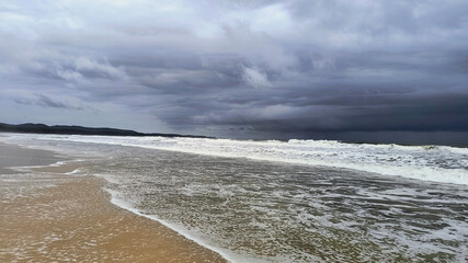 Stormy Ocean Waves Under a Dramatic Cloudy Sky at a Coastal Beach ocean waves rolling under an overcast stormy sky, with the sandy beach extending into the horizon, evoking feelings