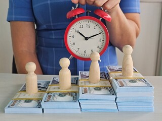 Time management represented through clock and wooden figures arranged on stacks of cash