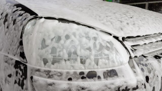 Black car full of detergent on the outside specially for cleaning cars. The process of professional cleaning of a car at a reputable car wash. Close-up image of details of how the detergent flows