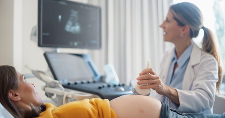 Young Pregnant Woman Lies on a Clinic Bed while a Female Obstetrician Performs an Ultrasound...