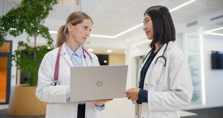 Diverse Female Physicians Collaborate in a Modern Hospital Lobby, Reviewing Patient Data on a...