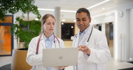 Diverse Medical Team Having a Conversation in a Hospital Lobby, Surrounded by Passing Patients and...