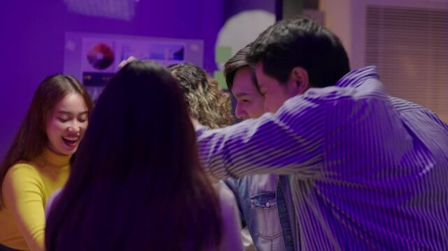 Young Asian business team stacking hands and raising them together and clasping hands after show of teamwork and success, celebrating their achievement with enthusiasm.