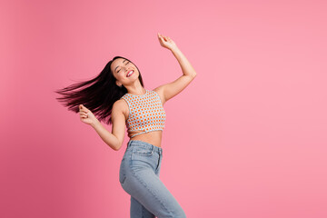 Joyful young asian woman with long brunette hair dancing against a vibrant pink background conveying happiness and freedom