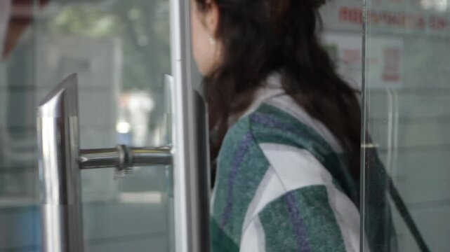 A young beautiful woman opens the glass door to an automated delivery point and walks in to pick up a package.