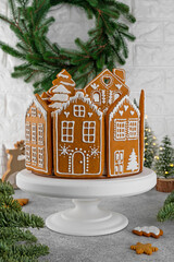 Honey Christmas cake decorated with gingerbread house cookies on a white cake stand. Festive dessert. Selective focus, copy space.