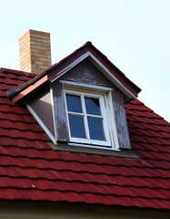 Detail of single old skylight window on an older rural vintage house with red shingles. So called dormer, Backlit, with white tones