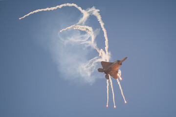 A fighter jet deploys countermeasure flares in the sky, leaving dramatic smoke trails during an...