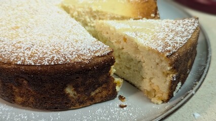 Freshly baked homemade cheesecake with a golden crust, dusted with powdered sugar, and served on a plate.