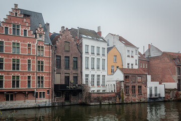 Naklejka premium Tradtitional brick and stone architecture buildings along a canal in Ghent Belgium. Photo taken on a cloudy day