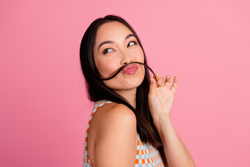 Playful young woman making a mustache with her hair against a pink background, embodying fun and...
