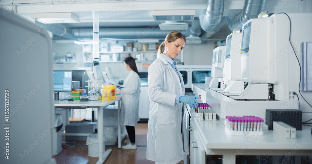 Poster Biomedical Researchers Conduct Experiments in a Modern Laboratory. Female Scientist Preparing a Set of Samples in Test Tubes with Purple Caps. Colleague Analyzes Data on a Computer in the Background