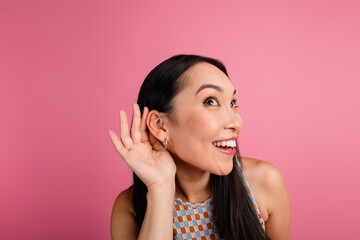 Joyful young woman listening with hand to ear against vibrant pink background, showcasing trendy...