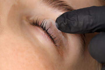 Esthetician cleaning woman's lashes after lamination procedure, closeup