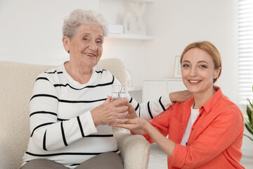 Obraz premium Caregiver giving glass of water to senior woman at home