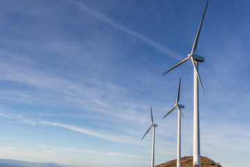Fototapeta premium Wind turbines generating green energy on mountain top under blue sky