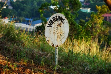 Oznaczenie znak który ostrzega przez zagrożeniem. Warning napis na znaku ostrzegawczym w trawie. © Adam