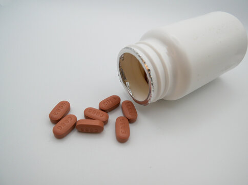 Un bote de pastillas blanco y abierto yace de lado con varias p&iacute;ldoras de color marr&oacute;n derramadas sobre un fondo blanco liso para un concepto m&eacute;dico