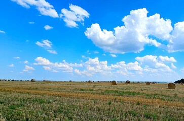 Farm landscape with hay bales under a vibrant blue sky filled with fluffy clouds in the countryside...