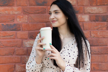 Stylish young woman enjoying a coffee moment against a red brick wall – lifestyle and fashion concept. 