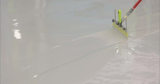 A builder distributes resin flooring material evenly using a Scraper Float. A builder is applying polymer floors using Scraper Float. The process of creating polymer floors