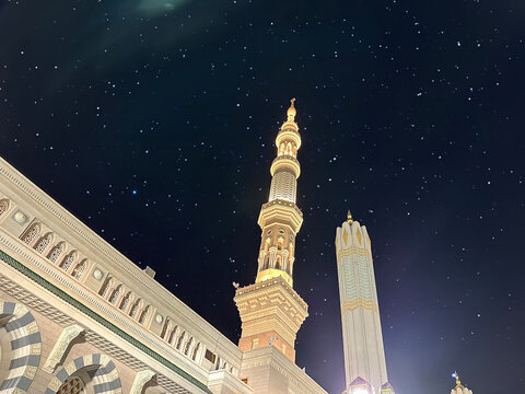 Night Al-Masjid an-Nabawi (Prophet's Mosque) in Medina city, Saudi Arabia against the background of the starry sky with place for text. Islamic background .