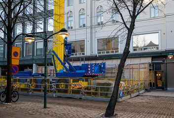Urban construction site with a blue crane, safety barriers, and road signs, set in front of a...